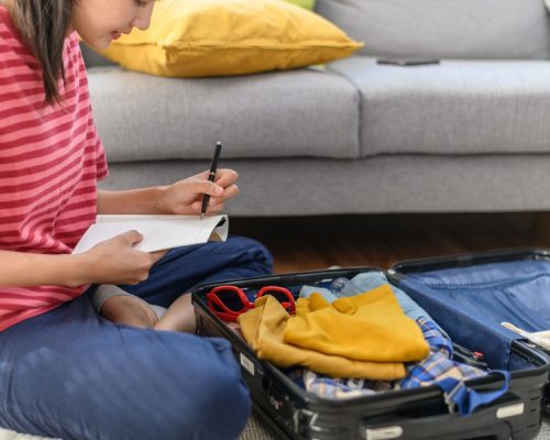 Jovem organizando roupas e itens essenciais, seguindo um checklist de viagem para se preparar antes de viajar.